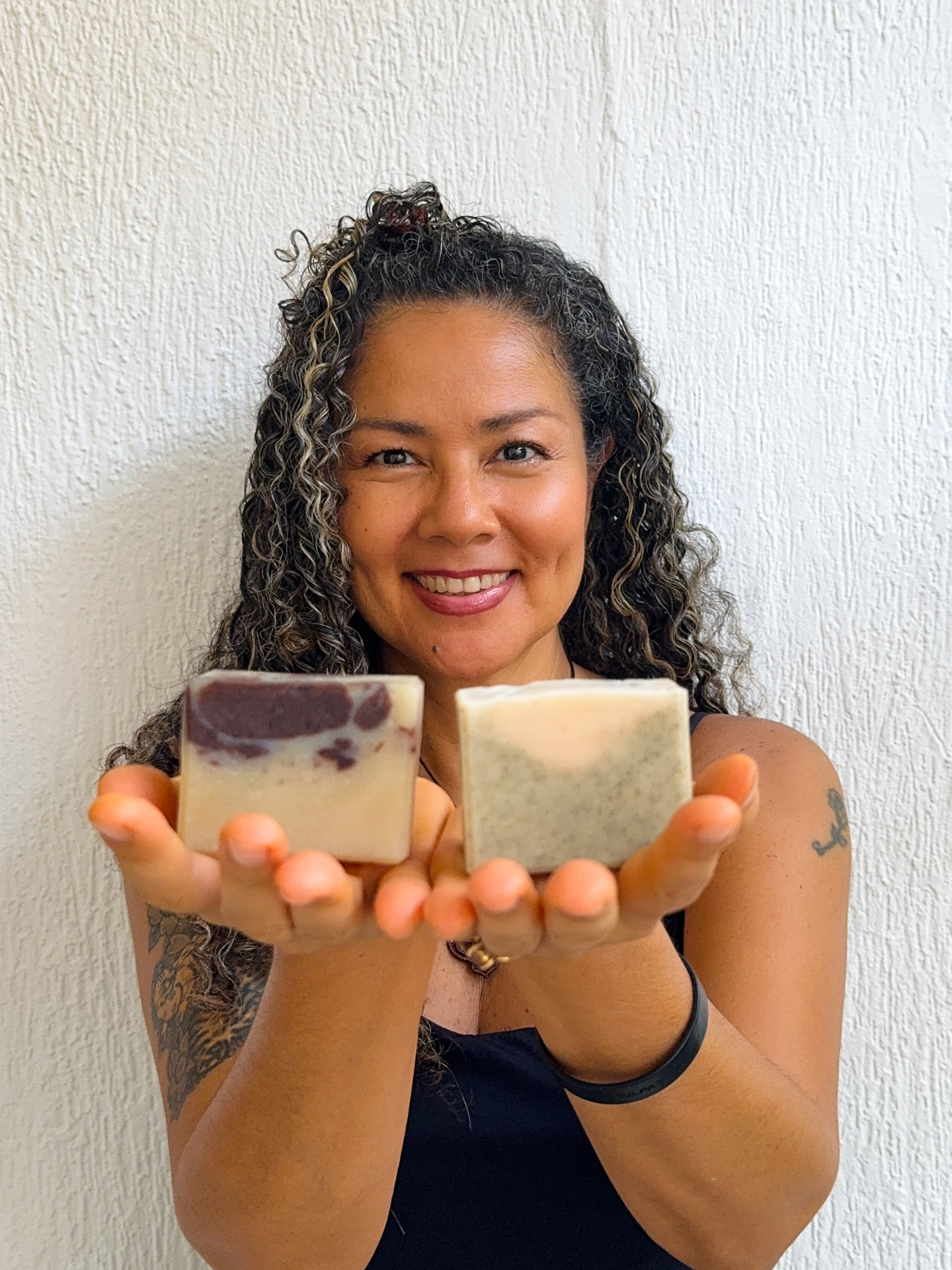 Sachi sorrindo e oferecendo dois sabonetes artesanais 100% naturais